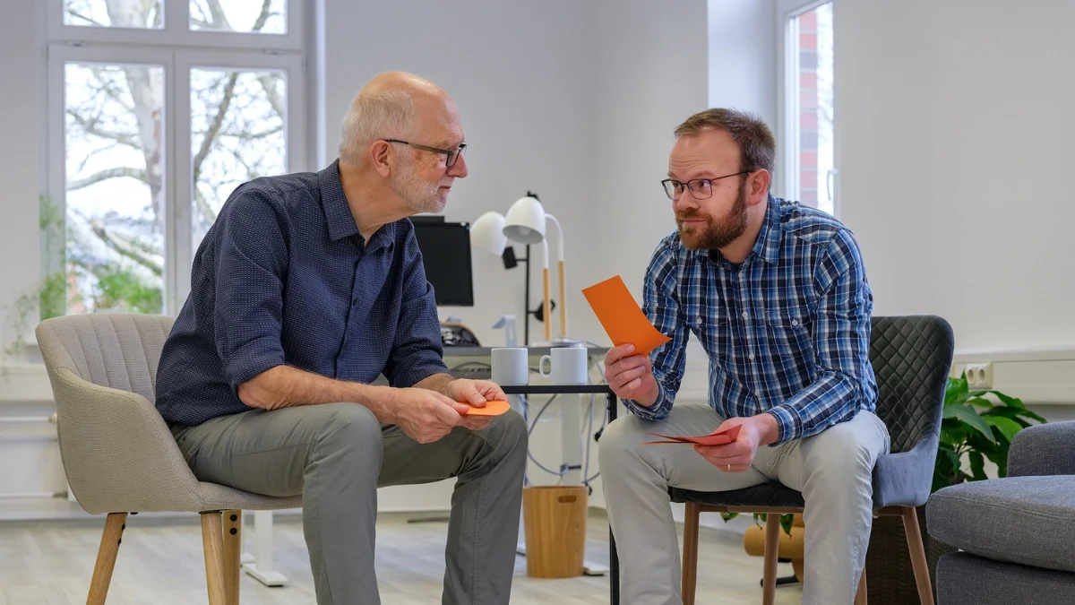 Zwei Männer sitzen im Gespräch, besprechen Unterlagen und reflektieren Inhalte gemeinsam in einem persönlichen Coaching- und Training-Setting.